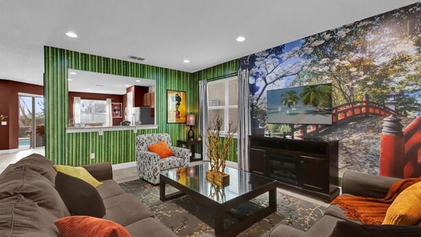 Una sala de estar moderna con una pared verde decorativa, un televisor de pantalla plana grande, una mesa de centro de vidrio y un sofá con muchos cojines.