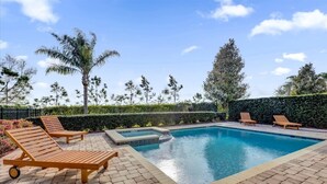 Una piscina rectangular con hidromasaje, rodeada de un patio de ladrillo y sillas de madera para relajarse.