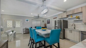 A modern kitchen with a dining area, featuring a central island, blue chairs, and a stainless steel refrigerator. - Beachfront with Rooftop Scenic Ocean View 2-bedroom (Saint Ann's Bay)