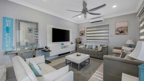 A modern living room with a sofa, armchairs, a coffee table, a TV, and a ceiling fan. - Beachfront with Rooftop Scenic Ocean View 2-bedroom (Saint Ann's Bay)
