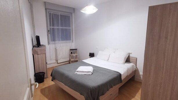 Une chambre à coucher comprenant un lit, une table de chevet, une lampe, une fenêtre et une armoire en bois.