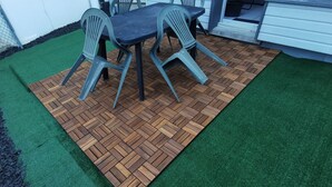 Un espace patio doté d’un plancher en bois disposé en motif de chevron, d’une pelouse artificielle verte et de chaises en plastique.
