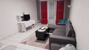 Un salon moderne avec un canapé gris, un meuble TV blanc et une table basse.