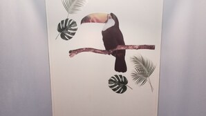 Une salle de bain comprenant des toilettes, un luminaire fixé au mur et un autocollant décoratif représentant un toucan perché sur une branche.