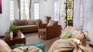A cozy living room with wicker furniture, a coffee table, and a view through a window with curtains.