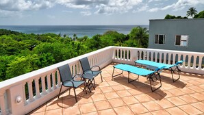A balcony with a table and chairs, overlooking a lush green landscape and the sea.
