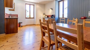 A kitchen with wooden cabinets, a dining table with chairs, and a window with blinds. - Gite ROSSANAZ - La compagnie du Bourg (LE CHATELARD)