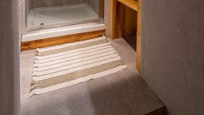 A shower area with a glass door, a wooden shelf, and a striped rug on the floor. - Gite ROSSANAZ - La compagnie du Bourg (LE CHATELARD)