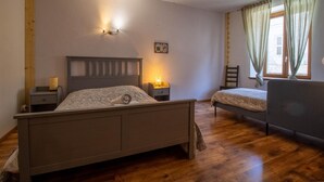 A bedroom with a wooden bed, a bedside table, a chair, and a window with curtains. - Gite ROSSANAZ - La compagnie du Bourg (LE CHATELARD)