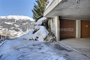 A snow-covered parking area with a concrete building and a mountain in the background. - Very comfortable studio for 2 people, living room with wood-burner, kitchen area with dishwasher, sl (Grimentz)