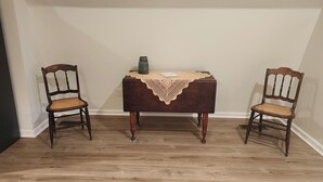 A room with a wooden floor, a small table with a lace tablecloth, and two wooden chairs with woven seats. - Brand new studio apartment with queen bed, queen pull out, WIFI and AC . (Wooster)