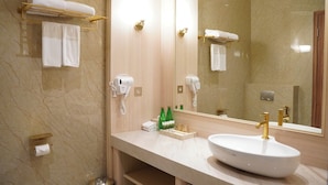 A bathroom with a marble wall, a sink with gold fixtures, a towel rack, and a mirror.
