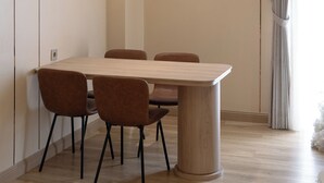 A dining area with a wooden table and four chairs, a light-colored floor, and a window with curtains.