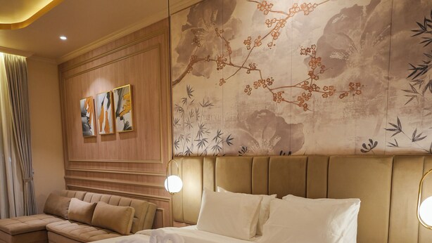 A hotel room with a large bed, a sofa, a wall with artwork, and a patterned carpet.