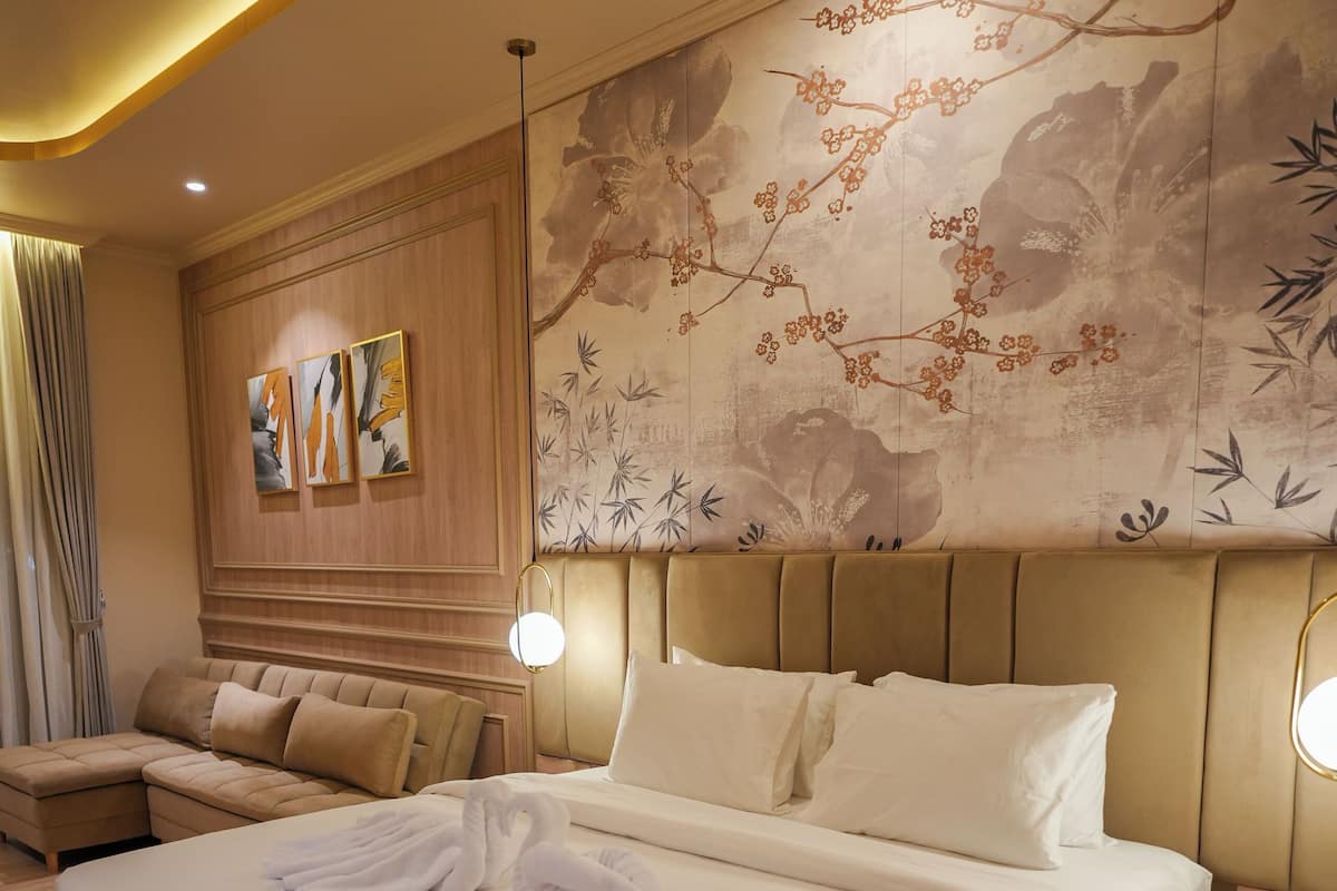 A hotel room with a large bed, a sofa, a wall with artwork, and a patterned carpet.