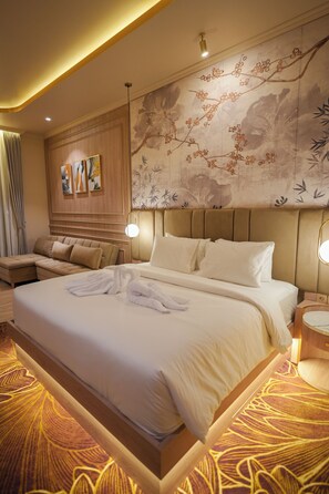 A hotel room with a large bed, a sofa, a wall with artwork, and a patterned carpet.