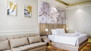 A hotel room with a bed, a sofa, a round wooden side table, and two wall-mounted paintings.