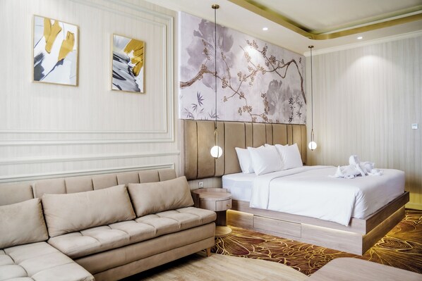 A hotel room with a bed, a sofa, a round wooden side table, and two wall-mounted paintings.