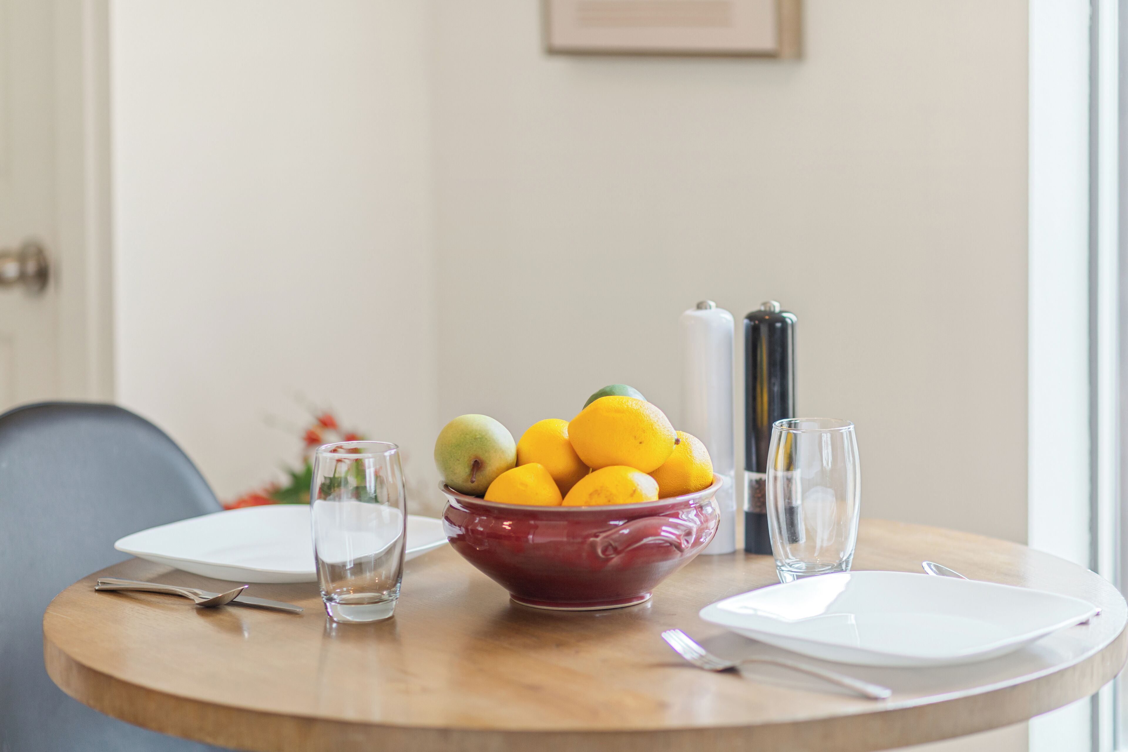 Una mesa de comedor con un frutero, una botella de vino y copas vacías.