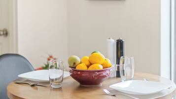 Una mesa de comedor con un frutero, una botella de vino y copas vacías.