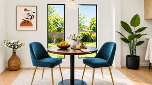 A dining area with a round table, two blue chairs, a vase with flowers, and a potted plant.