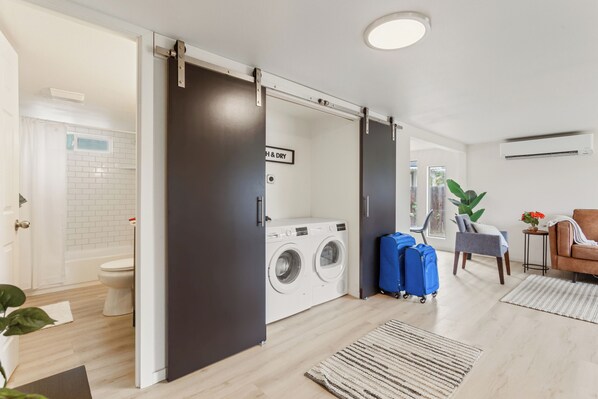 A modern apartment with a laundry area, a sliding door, a seating area with a chair, and a small table with a plant.