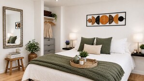 A neatly arranged bedroom with a bed, bedside tables, a mirror, and a wall art piece.