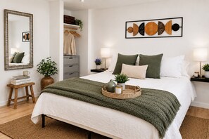 Un dormitorio ordenado con cama, mesitas de noche, un espejo y una obra de arte en la pared.