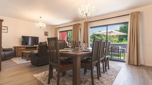 Un salón amplio con comedor, televisor y un gran ventanal con cortinas.