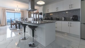 A modern kitchen with a large island, bar stools, and a dining area with a view. - Blue Outlook Retreat by Atlantic Holiday (Água de Pena)