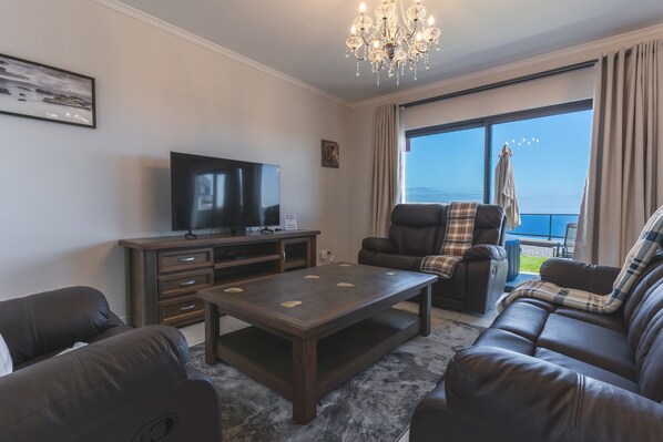 Una sala de estar con televisor, sofá, sillón reclinable, mesa de centro y un ventanal con vistas.