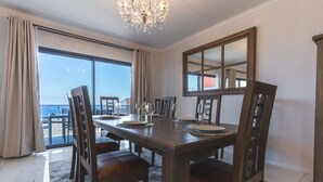 A dining area with a large table set for six, surrounded by wooden chairs. A chandelier hangs from the ceiling, and a large mirror is mounted on the wall. - Blue Outlook Retreat by Atlantic Holiday (Água de Pena)