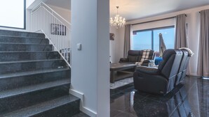 A modern living room with a black leather sofa, a massage chair, and a large window with curtains. - Blue Outlook View by Atlantic Holiday (Água de Pena)
