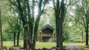 Eine Hütte mit Veranda, umgeben von Bäumen und einem Kiesweg.