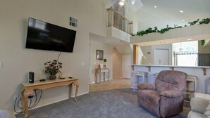 Een ruime woonkamer met een flatscreen televisie, een houten console tafel en een comfortabele fauteuil.