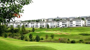 Een golfbaan met een clubhuis en woongebouwen op de achtergrond.