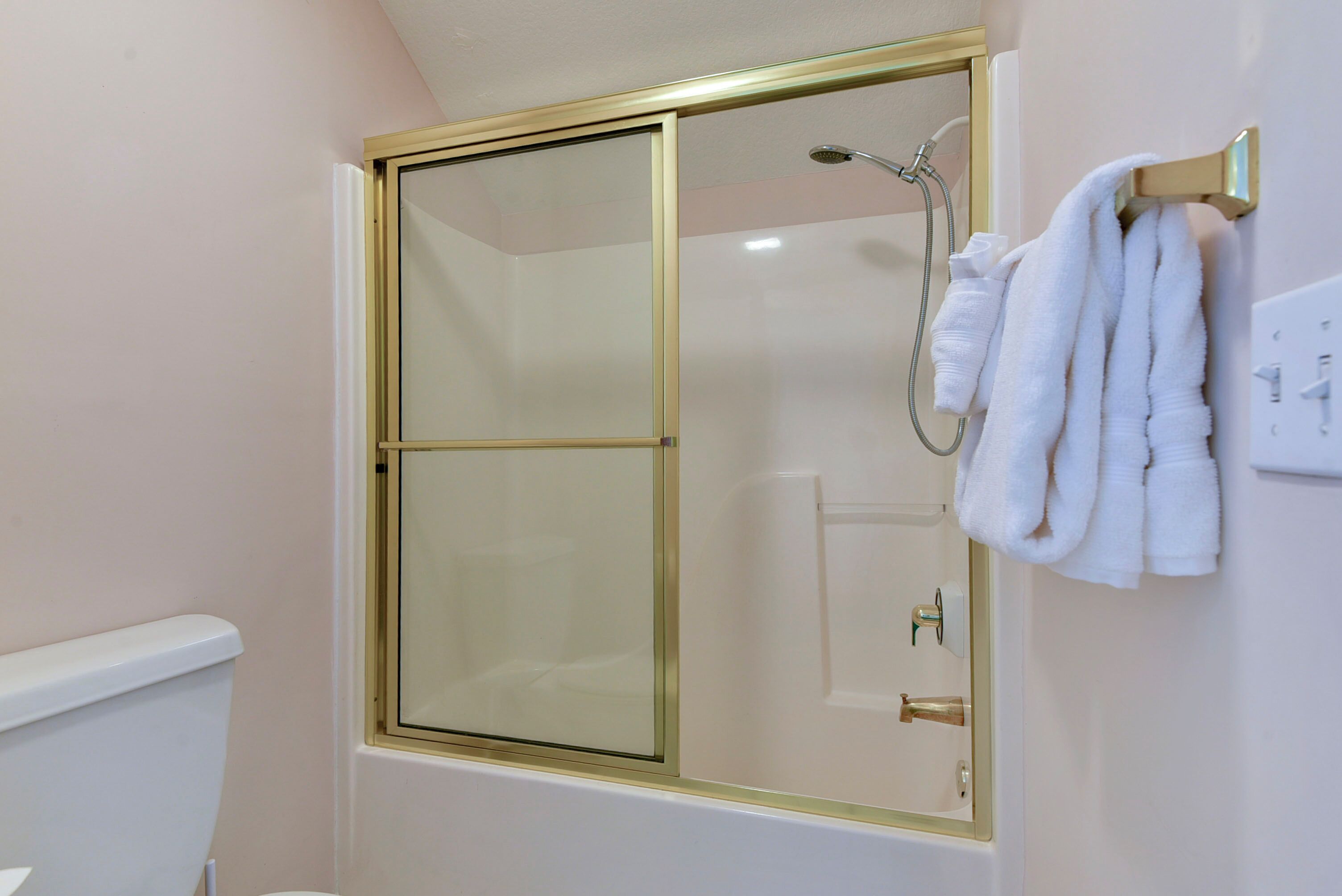 Et badeværelse med glasvæg omkring brusebad, toilet og et håndklædestativ med håndklæder.