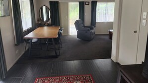 A spacious living area with a wooden dining table, a comfortable grey sofa, and a large mirror. - Ruru Retreat - peaceful oasis set off the road, pet friendly! (Coromandel)