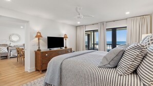 Une chambre avec un grand lit, une télévision, une commode et une vue sur la mer.