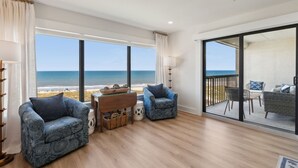 Une chambre avec vue sur la plage, comprenant deux fauteuils à motifs, une table en bois et un lampadaire.