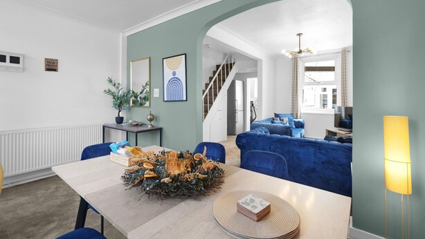 A dining area with a table set for four, a blue sofa in the background, and a staircase leading to another room.