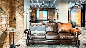 A spacious room with a leather sofa, a small side table, and a brick wall.