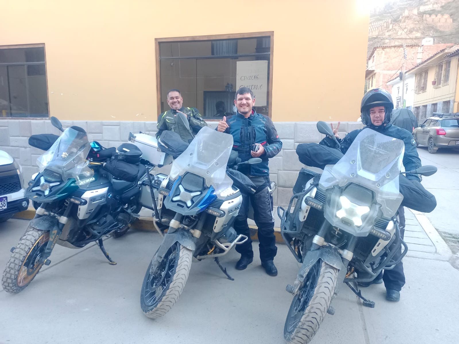 Three motorcycles parked in a row, a building with a sign, and a street with cars.