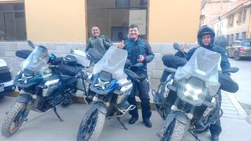 Three motorcycles parked in a row, a building with a sign, and a street with cars.