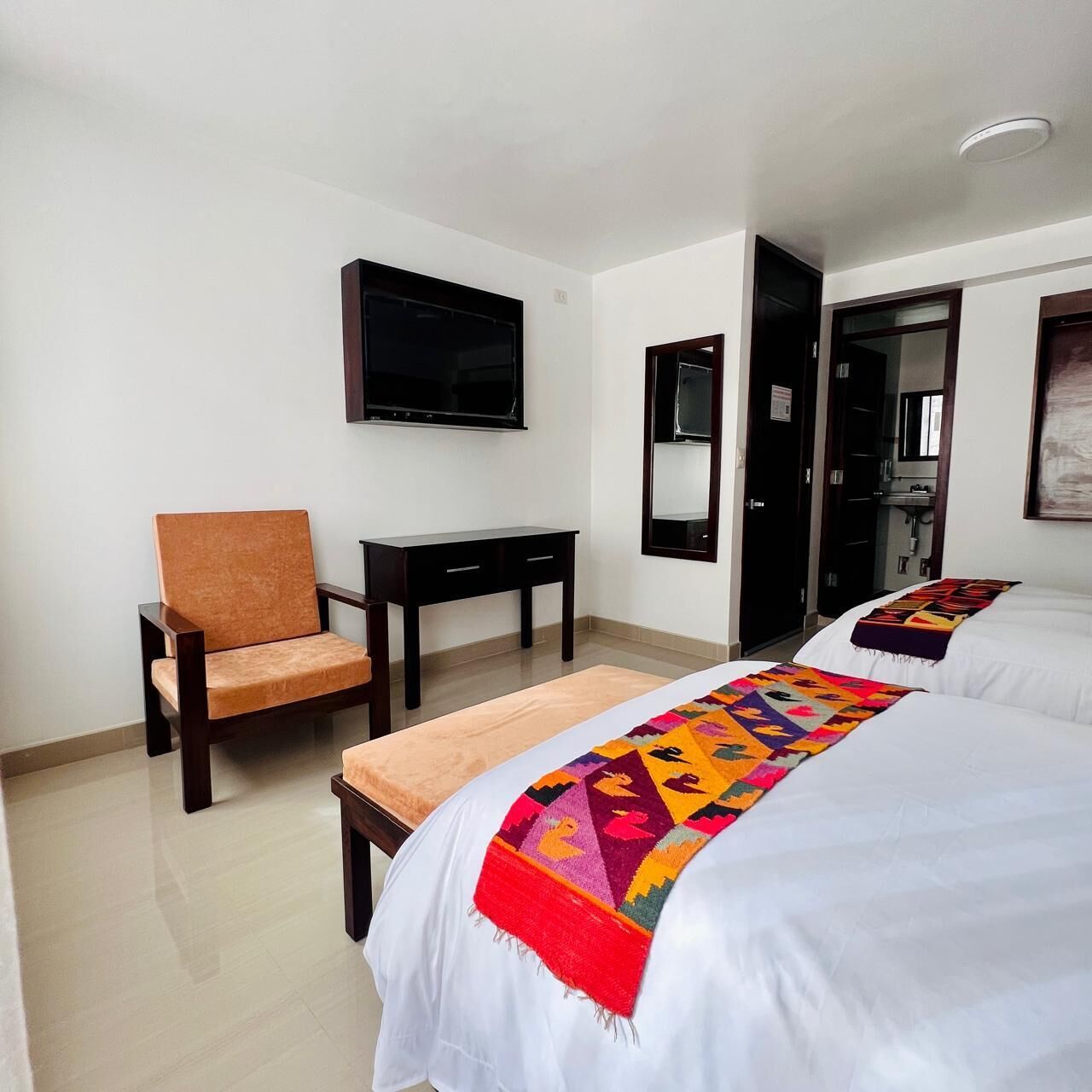A hotel room with two beds, a TV mounted on the wall, a desk, and a chair.
