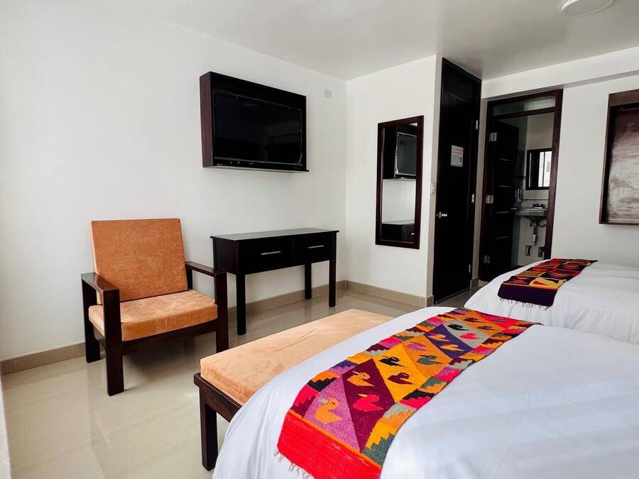 Habitación de hotel con dos camas, televisión montada en la pared, escritorio y una silla.