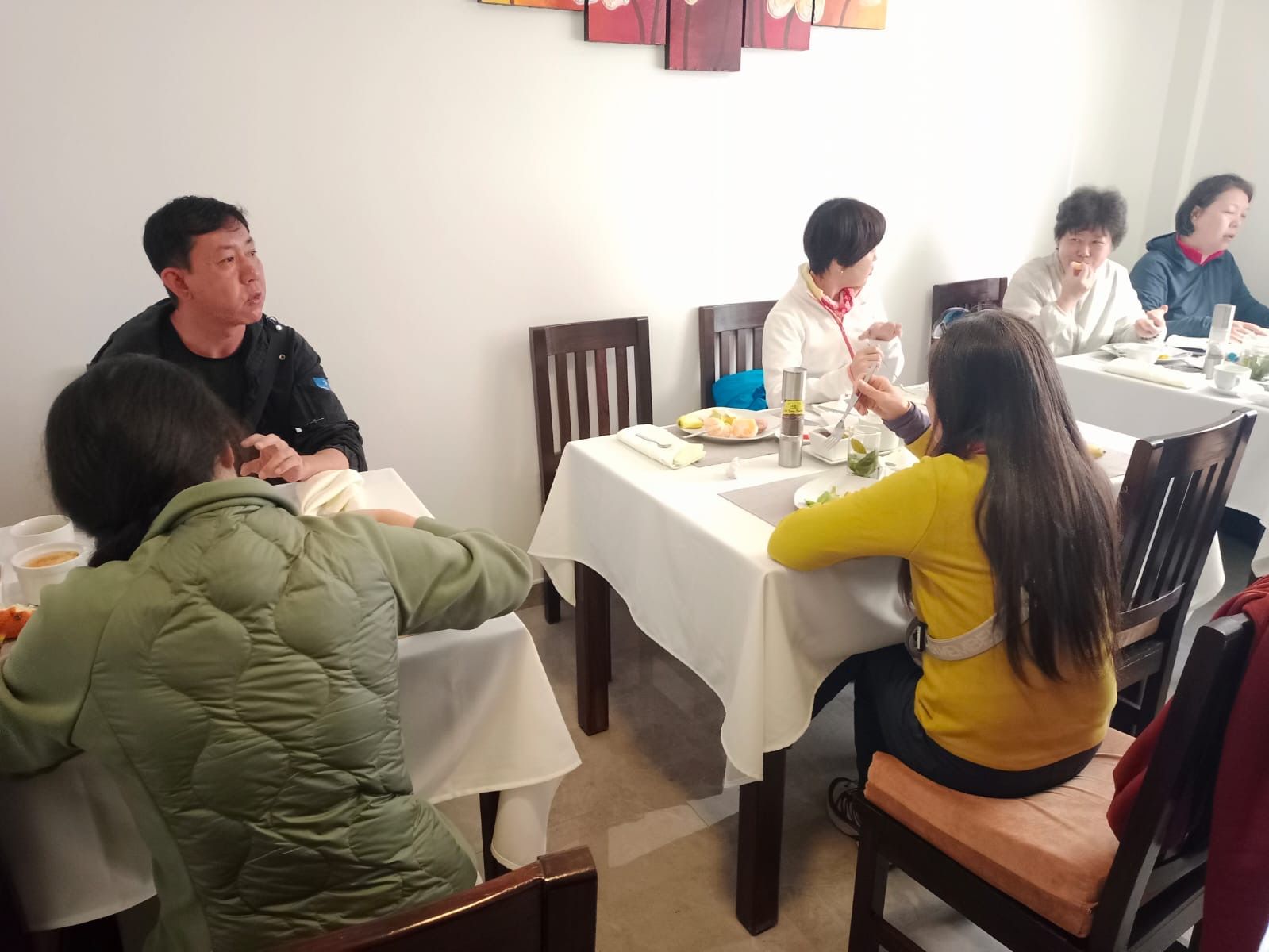 A group of people dining at a table with white tablecloths, wooden chairs, and a simple interior design.