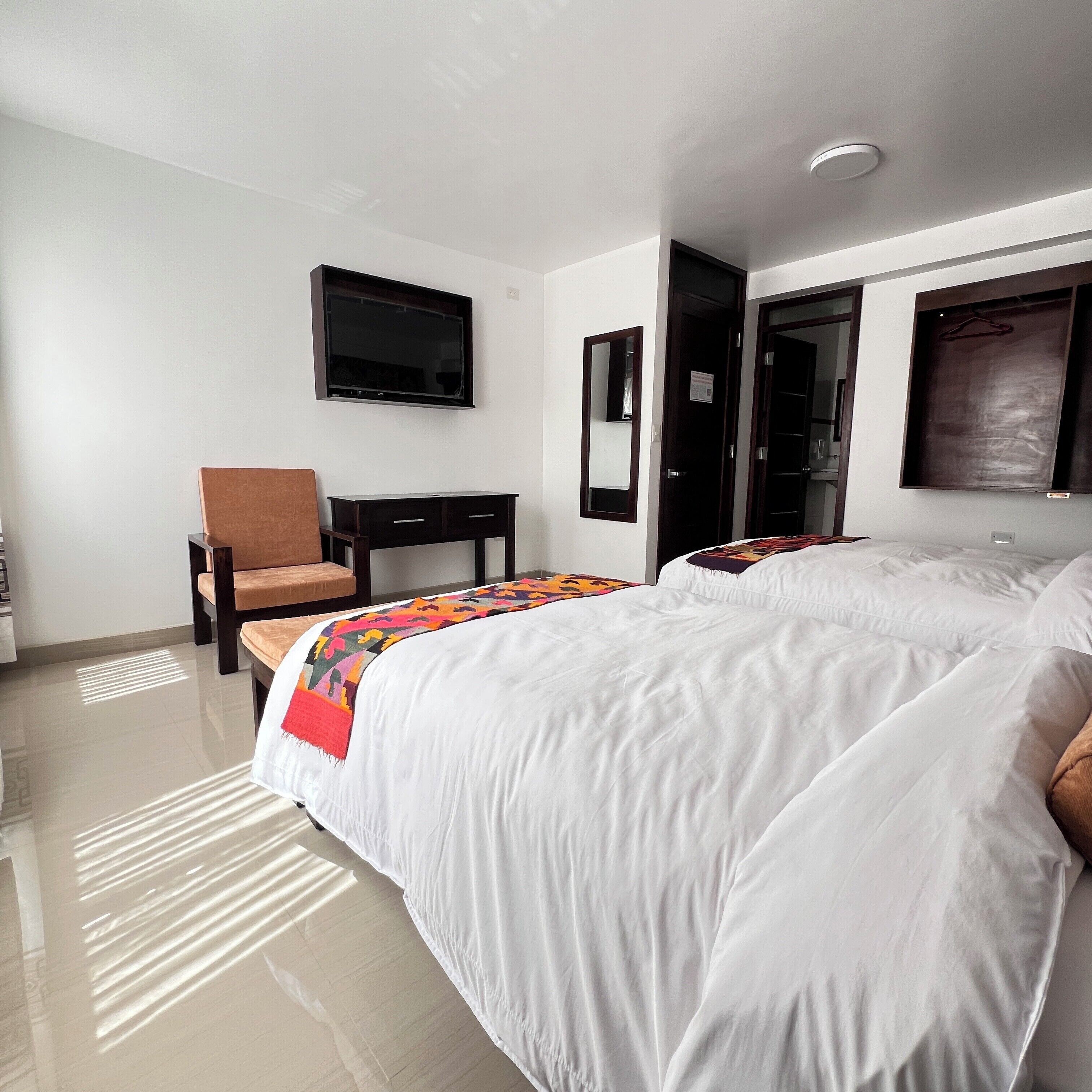 A hotel room with a bed, a desk, a chair, a TV, and a wardrobe.