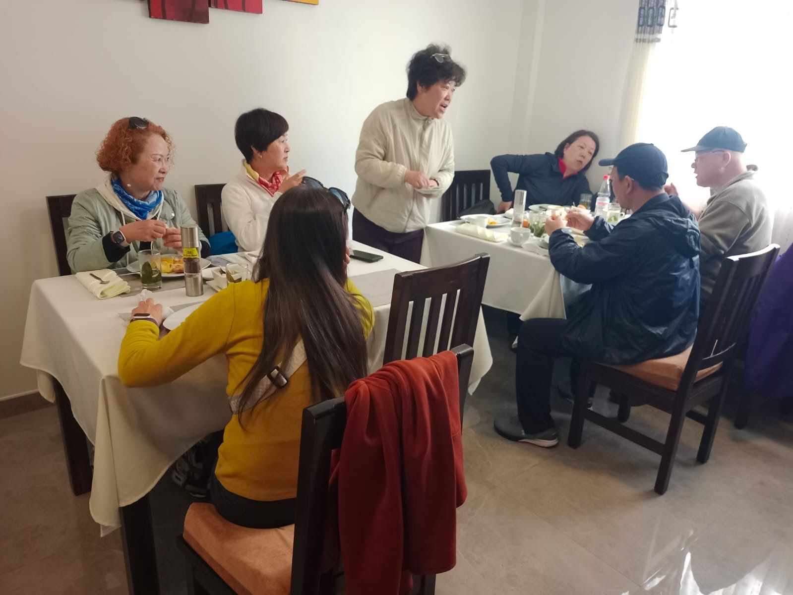Un grupo de personas sentadas alrededor de una mesa en un comedor, con sillas y un mantel blanco.