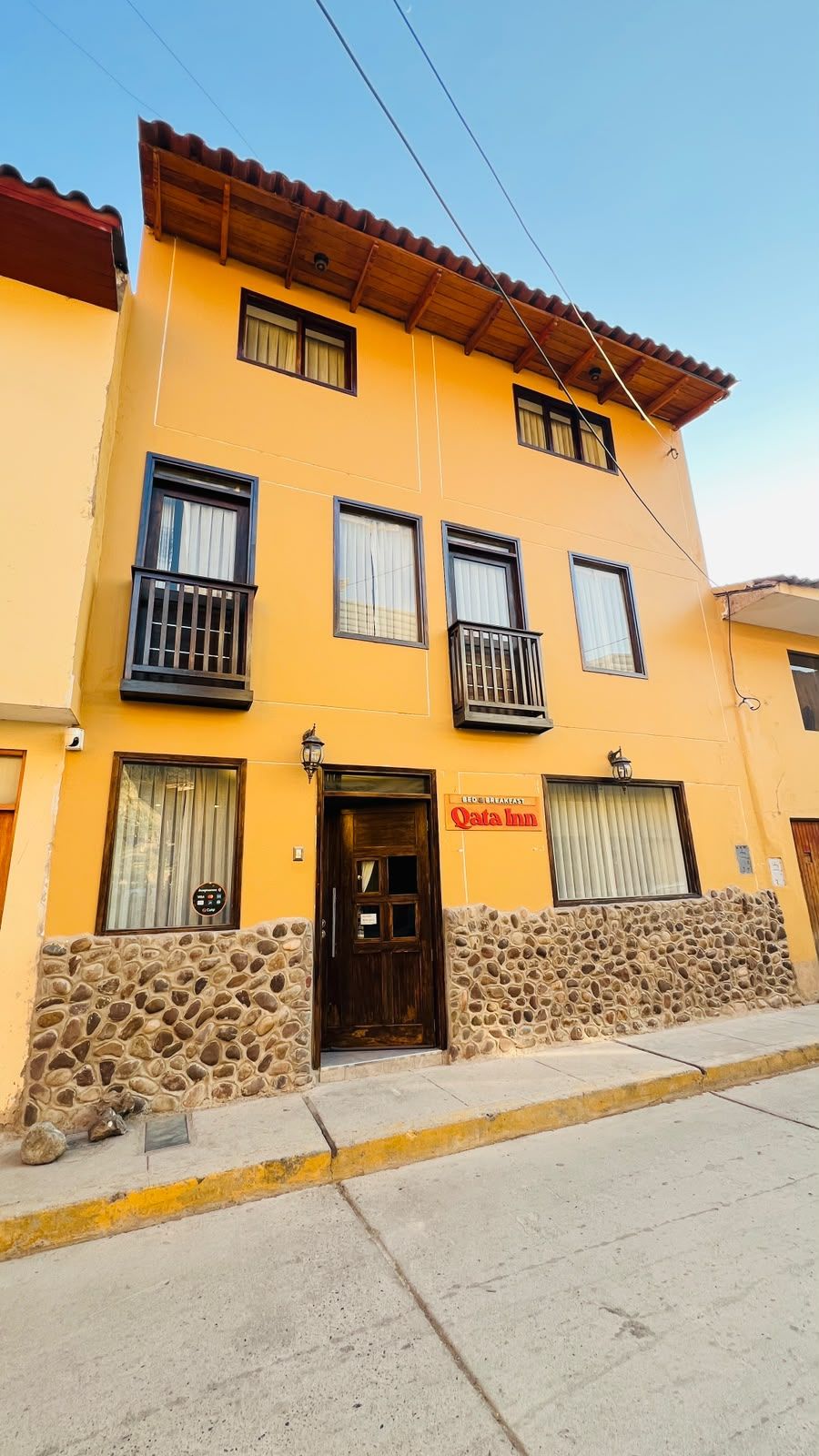 A two-story building with a stone facade, a sign for 'Qata Inn,' and a balcony on the second floor.
